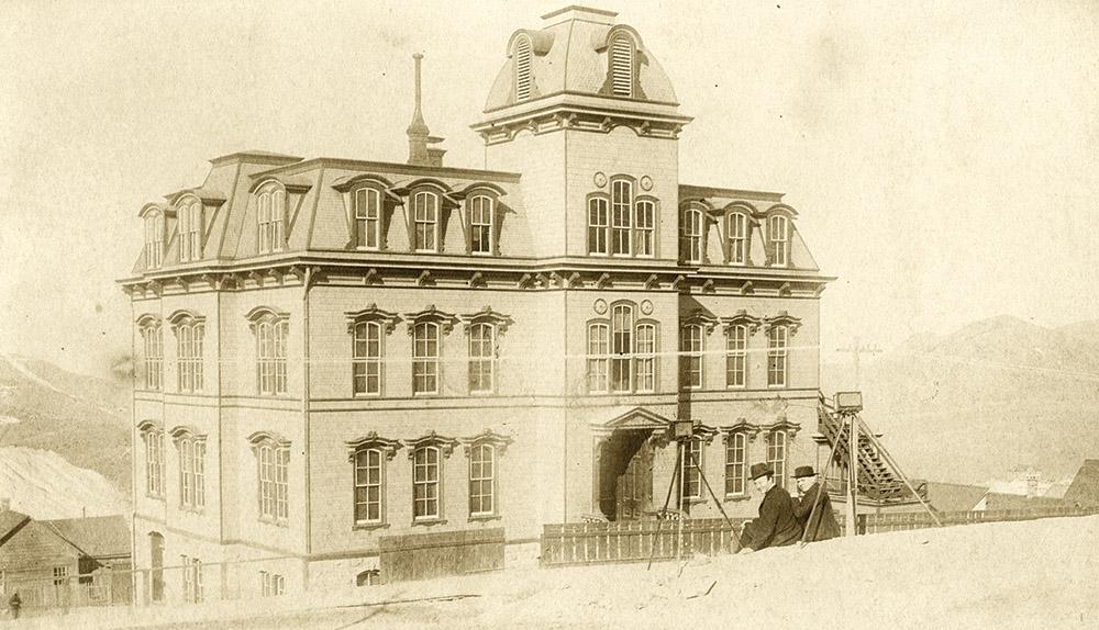The Fourth Ward School shortly after its completion, circa 1877, with two men and a surveying camera in the foreground