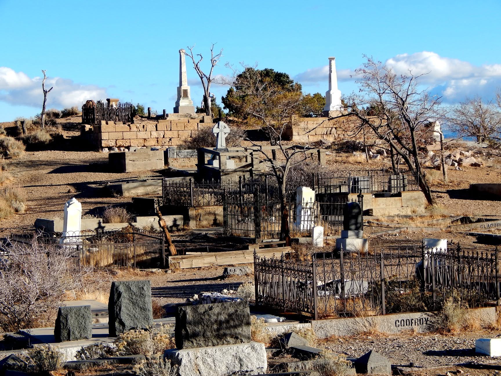 Wrought iron fences and Victorian headstones at Silver Terrace Cemetery in Virginia City, with obelisk monuments visible on the hillside