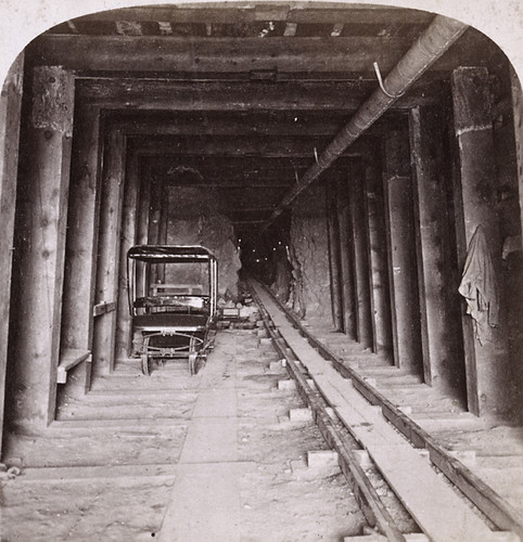 Interior view of the Sutro Tunnel showing heavy timber sets, rails, and a small ore car
