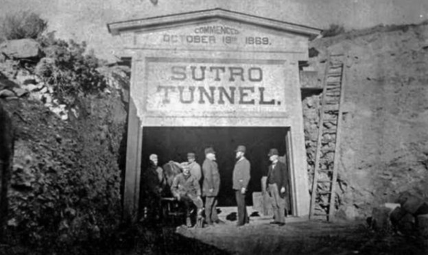 The Sutro Tunnel portal in the 1870s, inscribed Commenced October 19th 1869, with a group of men standing at the entrance