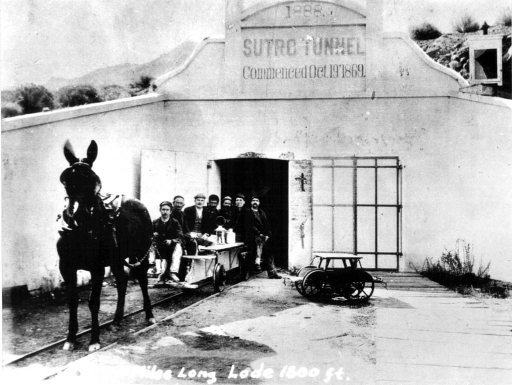 Later photograph of the Sutro Tunnel portal with a horse-drawn cart, workers, and rail equipment