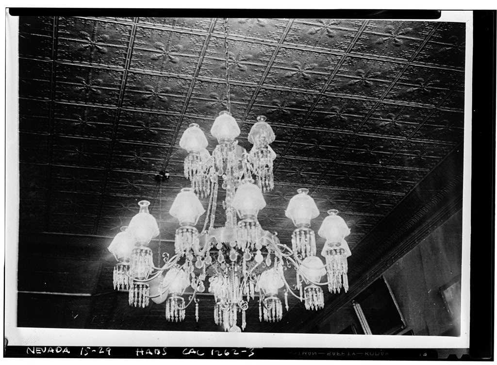 Black and white 1940 close-up photograph of a large tiered crystal chandelier beneath an embossed tin ceiling